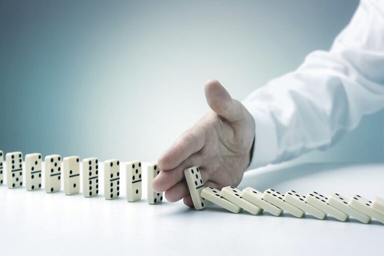 chaine de dominos et main bloquant leur chute pour illustrer la gestion des risques dans une période de crise dans une supply chain par l'experte de gestion des risques supply chain Katia Gutknecht
